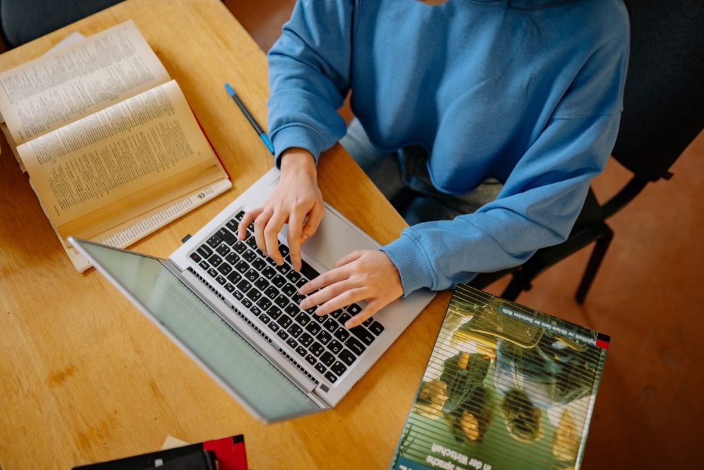 Hands working on a laptop beside open reference books