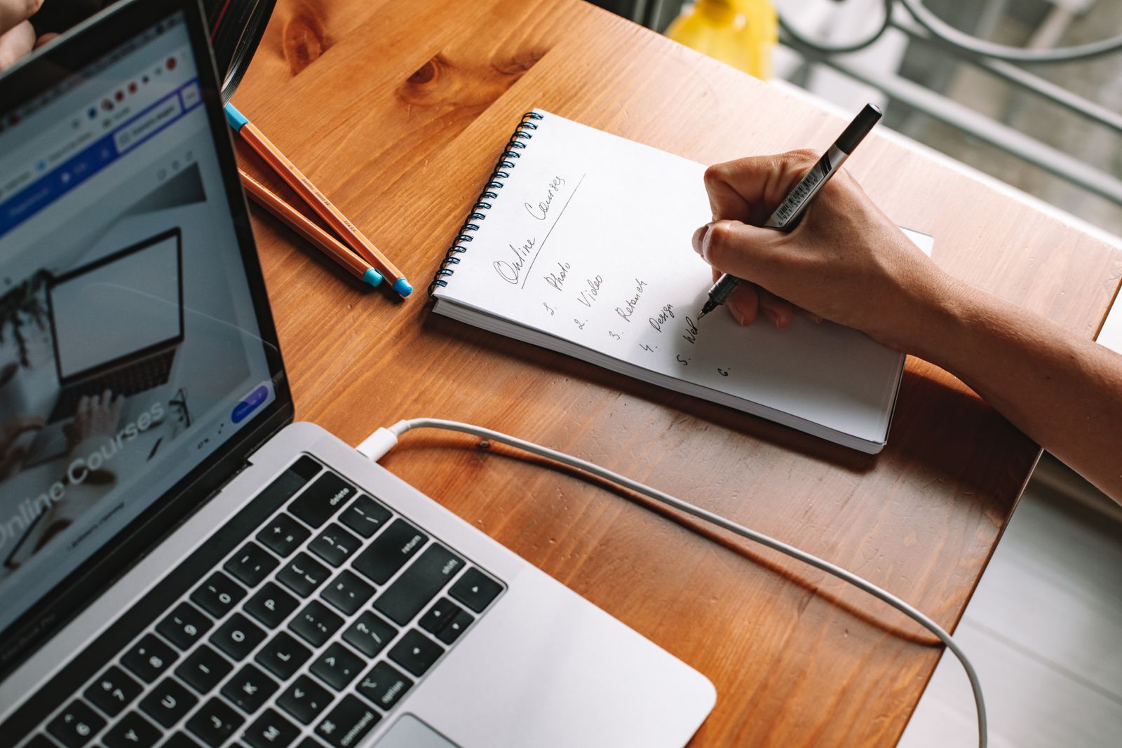 Notes being written beside a laptop during online research